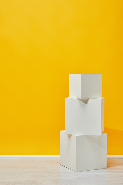 Minimalistic white plaster cubes arranged vertically near yellow wall - Foto, afbeelding
