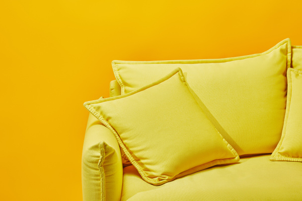 κοντινό πλάνο του φωτεινό καναπές με μαξιλάρια που απομονώνονται σε κίτρινο - Φωτογραφία, εικόνα