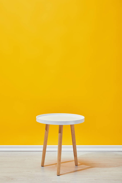 Tavolino minimalista in legno vicino alla parete gialla
 - Foto, immagini