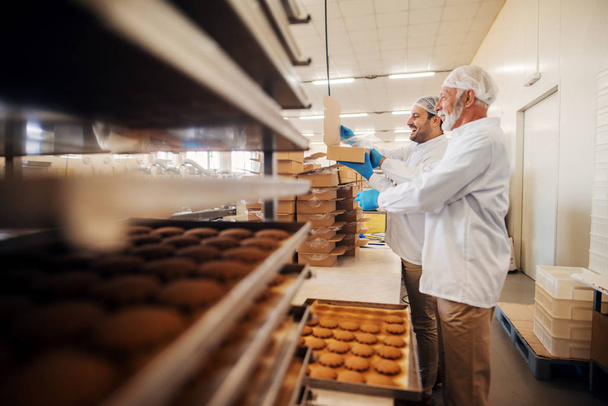 Arbeiter verpacken Kekse in Kartons, während sie in der Lebensmittelfabrik stehen. - Foto, Bild