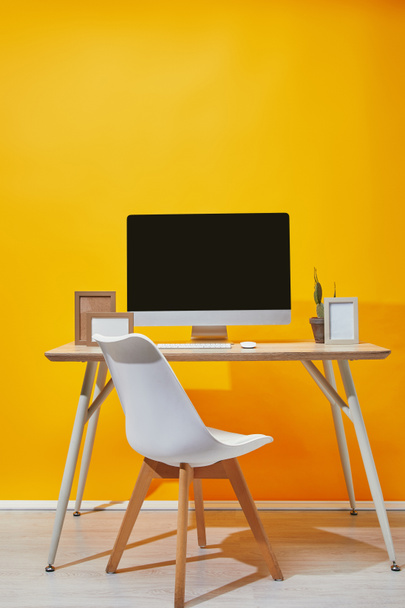 Computer, photo frames and cactus on workplace with yellow wall at background - Foto, Bild