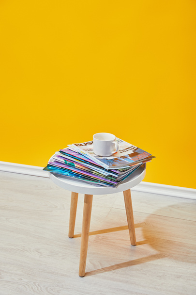 mesa de centro con revistas y taza blanca cerca de la pared amarilla
 - Foto, imagen