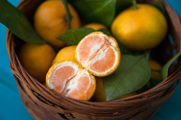 mandarijnen of mandarijnen met bladeren in mand op turquoise houten achtergrond - Foto, afbeelding