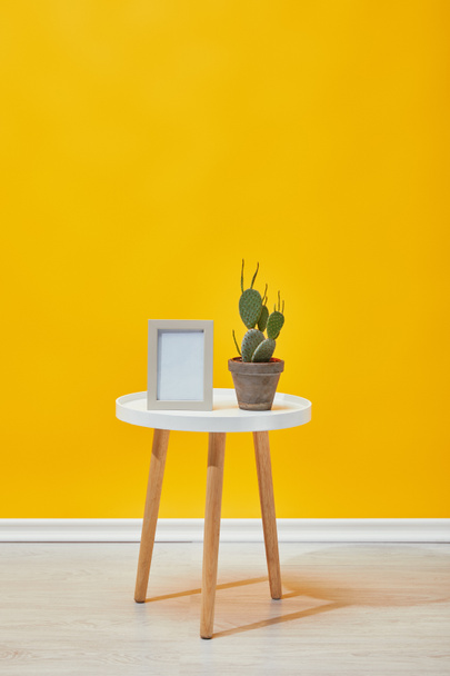 Cactus et cadre photo sur la table basse près du mur jaune
 - Photo, image