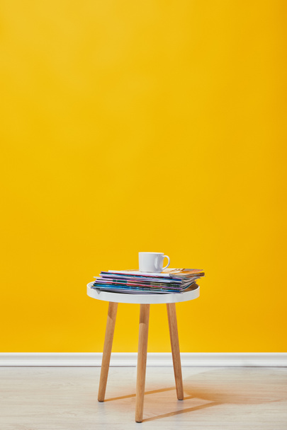 Little coffee table with journals and cup of coffee near yellow wall  - Photo, Image