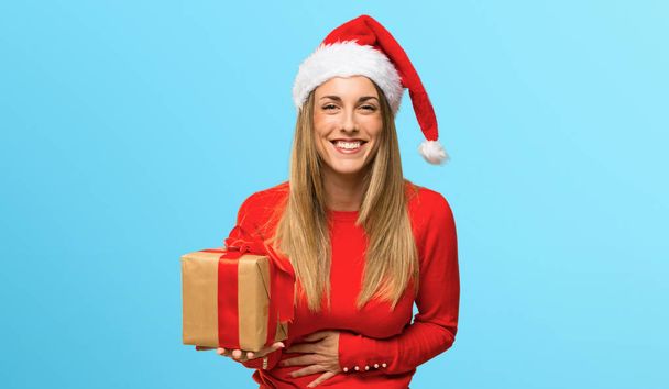 Femme blonde habillée pour les vacances de Noël souriant beaucoup tout en mettant la main sur la poitrine sur fond bleu
 - Photo, image
