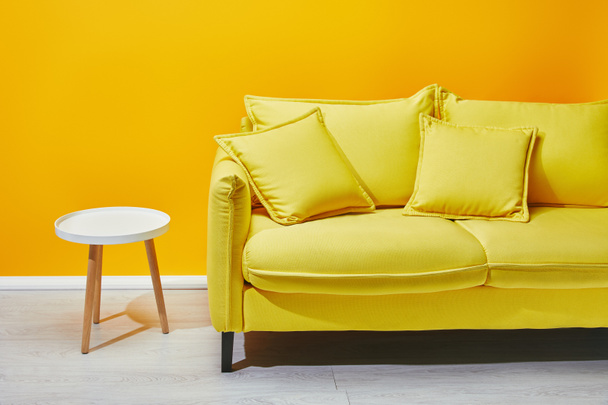 Желтый диван и белый журнальный столик возле яркой стены
 - Фото, изображение