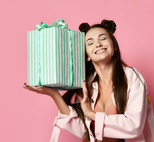 Portrait of an excited cute girl in jaket holding present box isolated over pink background - Fotó, kép