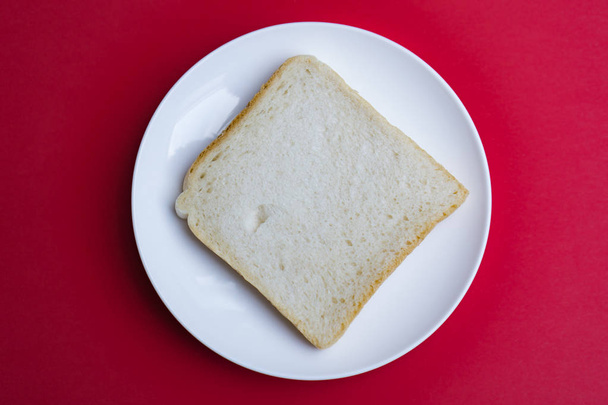 Кусок тоста на белой тарелке, красный фон
  - Фото, изображение
