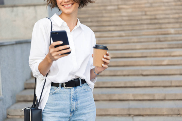 Cropped photo of young amazing woman on the street using mobile phone holding coffee. - Photo, Image