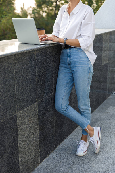 Cropped photo of young cute beautiful woman walking outdoors using laptop computer. - Фото, изображение