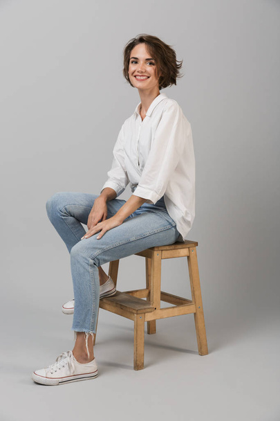 Image of young business woman posing isolated over grey wall background sitting on stool. - Photo, image
