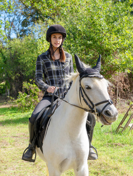 Mujer joven con casco negro montando un caballo blanco
 - Foto, imagen