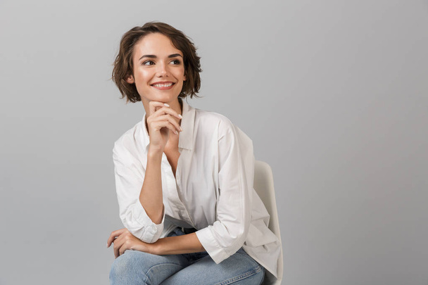 Image of young business woman posing isolated over grey wall background sitting on stool. - Fotoğraf, Görsel
