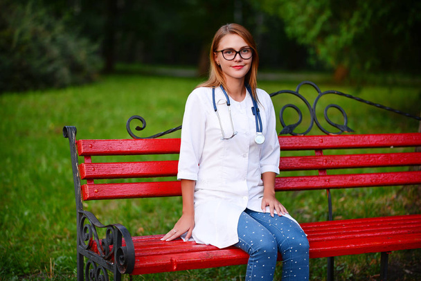 Młoda dziewczyna, która jest lekarzem stoi poza, siedzi na ławkach w pobliżu szpitala - Zdjęcie, obraz