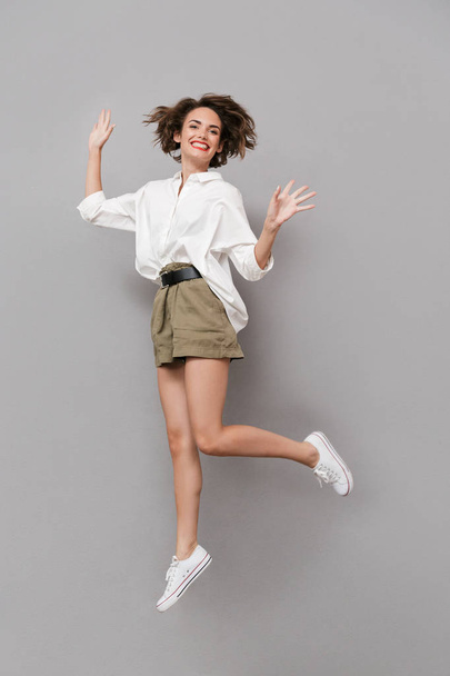 Full length image of european woman 20s smiling and jumping isolated over gray background - Valokuva, kuva