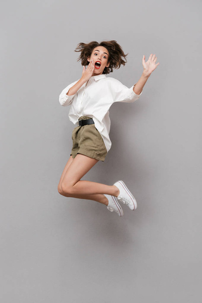 Full length image of young girl 20s smiling and jumping isolated over gray background - Foto, Bild