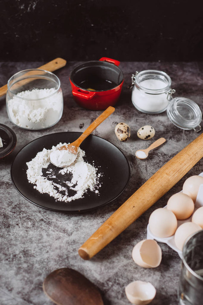 Ingredients and utensils for baking. Spoon with flour, dishes, eggs,  butter salt and rolling pin on a grey background. Flat lay.  - Foto, imagen