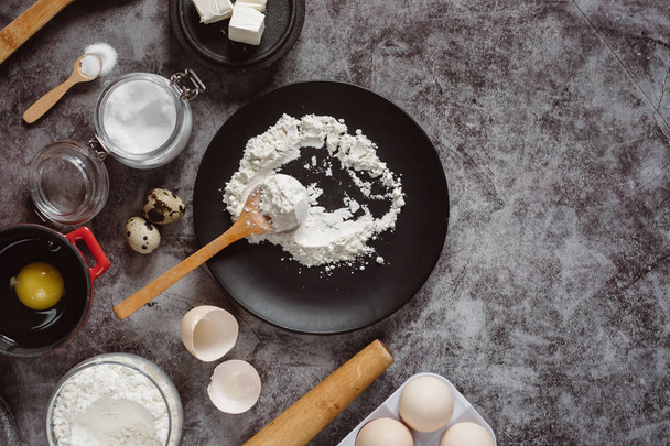 Ingredients and utensils for baking. Spoon with flour, dishes, eggs,  butter salt and rolling pin on a grey background. Flat lay. Text space - Photo, image