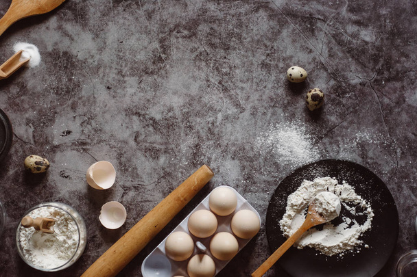 Ingredients and utensils for baking. Spoon with flour, dishes, eggs,  butter salt and rolling pin on a grey background. Flat lay. Text space - Foto, imagen