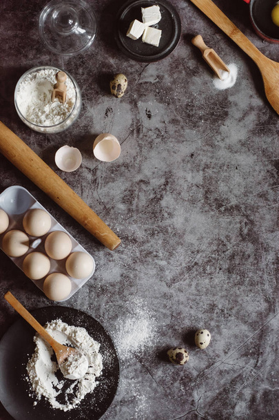 Ингредиенты и посуда для выпечки. Ложка с мукой, посуда, яйца, соль масла и скалка на сером фоне. Плоский лежал. Текстовое пространство
 - Фото, изображение