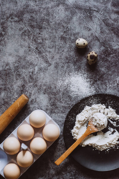 Ingredients and utensils for baking. Spoon with flour, dishes, eggs,  butter salt and rolling pin on a grey background. Flat lay. Text space - 写真・画像