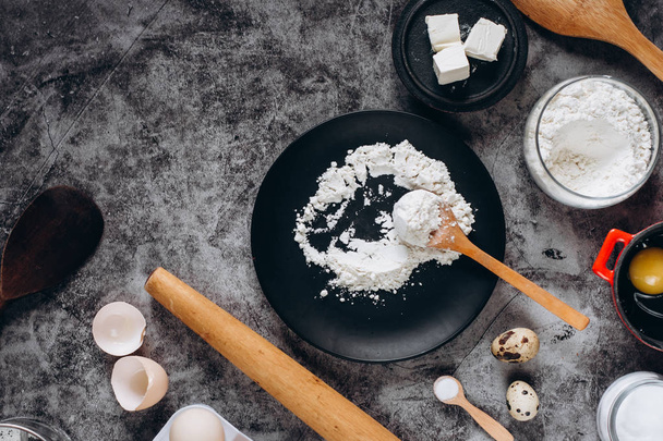 Ingredients and utensils for baking. Spoon with flour, dishes, eggs,  butter salt and rolling pin on a grey background. Flat lay. Text space - Zdjęcie, obraz