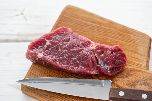 Raw meat. Raw fresh beef steak on a wood cutting board and Carving knife. White wooden background, top view, copy space, Daylight - Фото, изображение