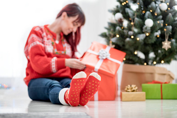 Feet in woolen socks by the christmas tree, woman looking at gift boxes - Φωτογραφία, εικόνα