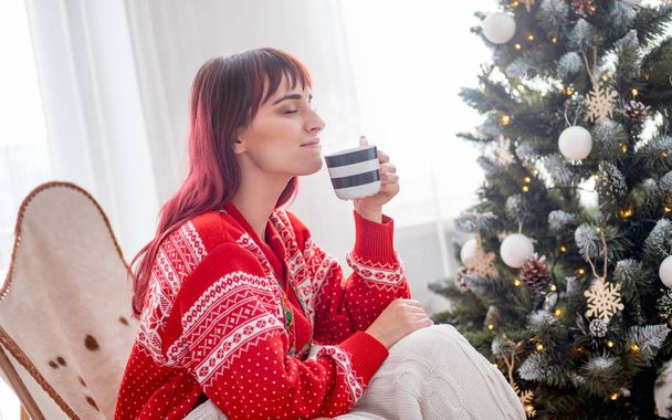 ホット コーヒーやクリスマス ツリーの横にある紅茶とリラックスした美しい女性 - 写真・画像