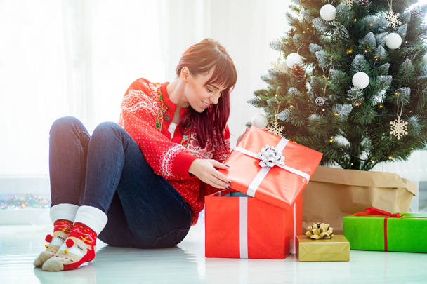 Smiling beautiful woman looking at gift boxes under christmas tree - Zdjęcie, obraz