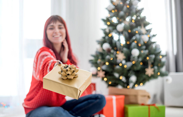 Smiling woman giving christmas gift box to camera - Foto, afbeelding