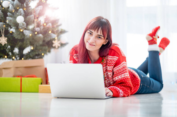 Smiling woman using laptop to Christmas shopping online lying on floor next to xmas tree - Foto, Imagem