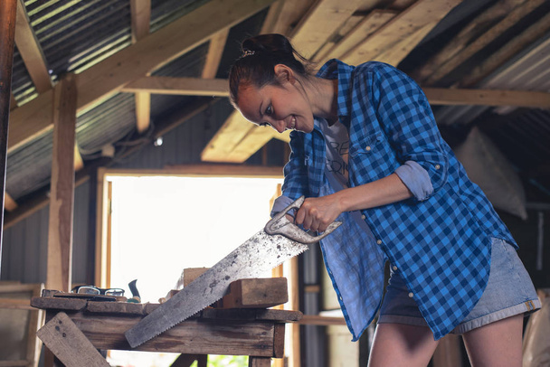 jeune femme avec une scie à métaux dans ses mains planches à scier dans l'atelier à la maison
 - Photo, image