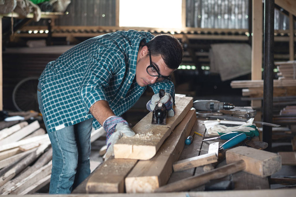 Man in plaid shirt and jeans planing wood manual planer in the workshop - Photo, Image