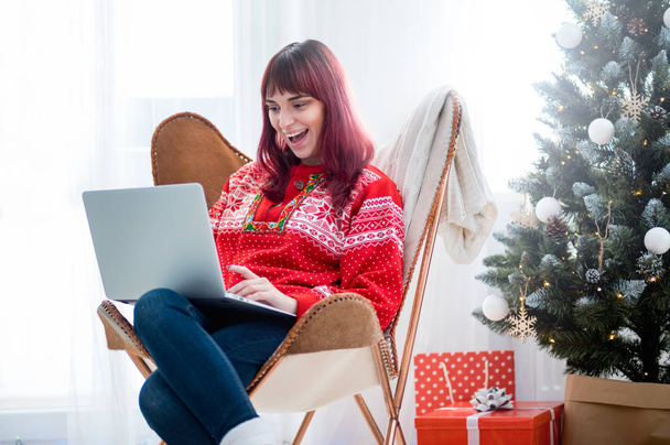 Young woman using laptop next to xmas tree, Christmas shopping online - 写真・画像