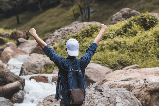 Back view of cheerful Asain traveler man raising hands outdoors scenic mountain background. Travel relaxation and successful concept. - Photo, Image