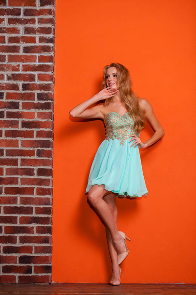 Full body portrait of a beautiful young blonde woman in a turquoise dress. Studio isolated on orange background - Fotografie, Obrázek