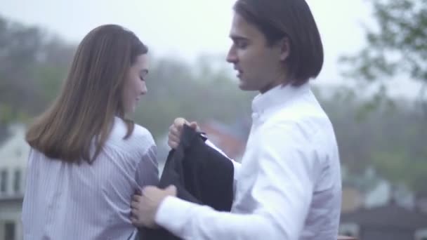 Handsome male puts his jacket on the female shoulders Guy and girlfriend spending time together Couple in love - Materiał filmowy, wideo