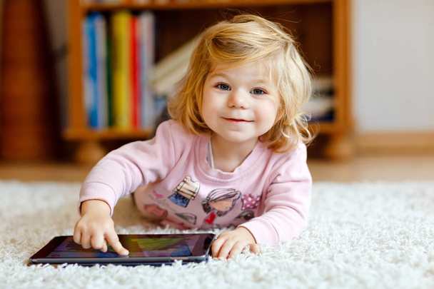 かわいい小さな幼児女の子がタブレット pc を自宅で遊んで。健康な赤ちゃんの指をパッドに触れて、漫画を見て、コンピューターの教育的なゲームを楽しんでいます。初期の開発コンセプト - 写真・画像