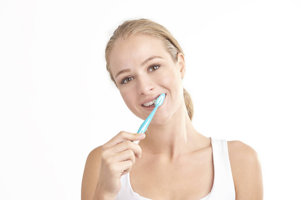 Studio shot of beautiful young woman brushing her teeth while looking at camera and smiling. Isolated on white background.  - Фото, изображение