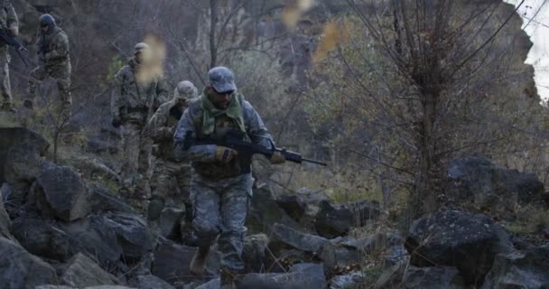 Bewaffnete Soldaten gehen in der Abenddämmerung durch Felsen - Filmmaterial, Video