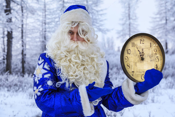 クリスマスのテーマ、販売、雪の森の中のハッピーサンタクロース、冬の森の背景にあるサンタ、ロシアのサンタ(祖父フロスト) 、サンタの手の時計は5分から12分を示しています - 写真・画像