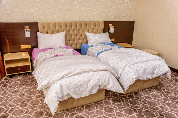 Interiér ložnice s krásným postelemi a ložním prádlem. Samostatná postel růžové a modré. Dvojlůžka s bílou a barvu listů. béžový interiér. měkké poduishi deky - Fotografie, Obrázek
