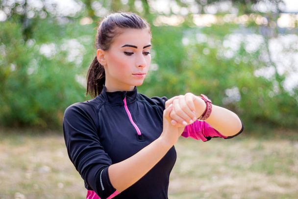 Jeune fille de fitness vérifie chronomètre tracker sur son poignet pendant la course en plein air - Photo, image