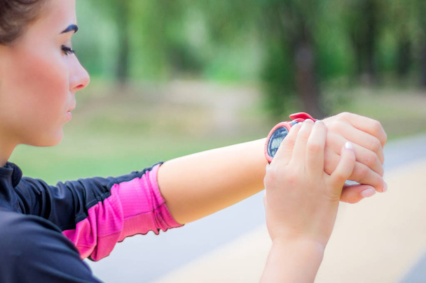 Joven chica de fitness comprueba el rastreador de cronómetro en su muñeca durante el funcionamiento al aire libre - Foto, imagen
