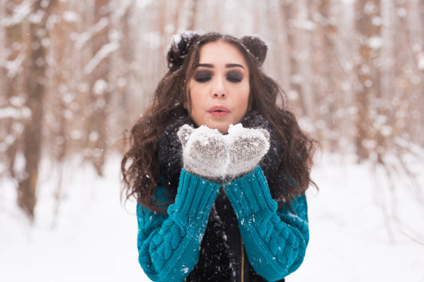 Noël, vacances et concept de saison - Jeune femme brune heureuse soufflant de la neige en hiver nature
. - Photo, image