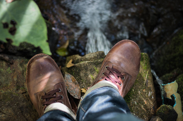 Chaussures en cuir marron Pivoter sur des rochers Le fond de la roche est une cascade
. - Photo, image