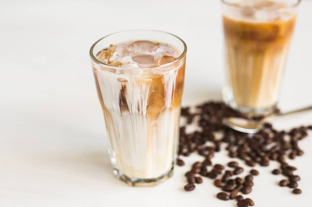 Кофе со льдом в стакане со сливками и кофейными зернами на столе
 - Фото, изображение