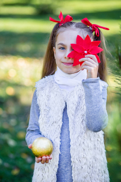 Cute girl decorating the Christmas tree outdoors in the yard before the holidays. Merry Christmas and happy holidays. - Foto, Imagem